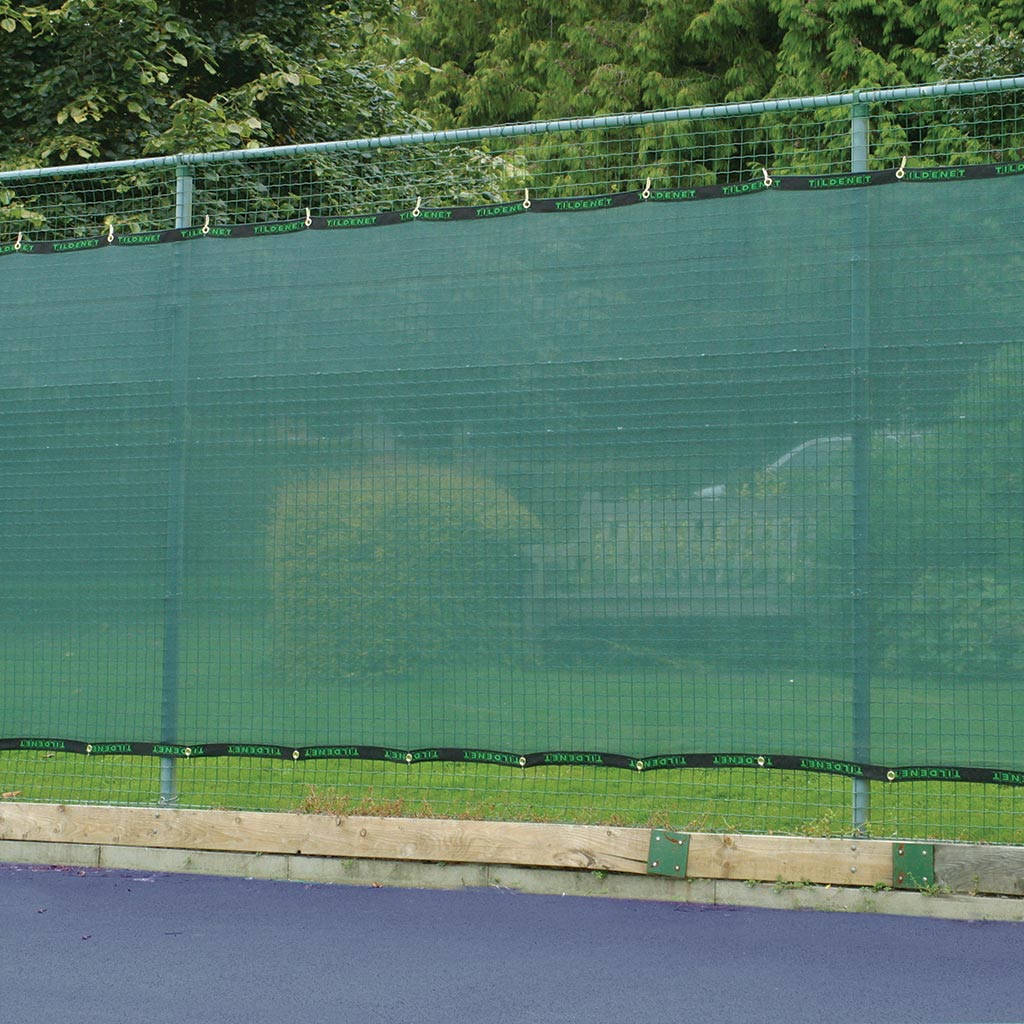 Tennis court with green fence and trees in the background