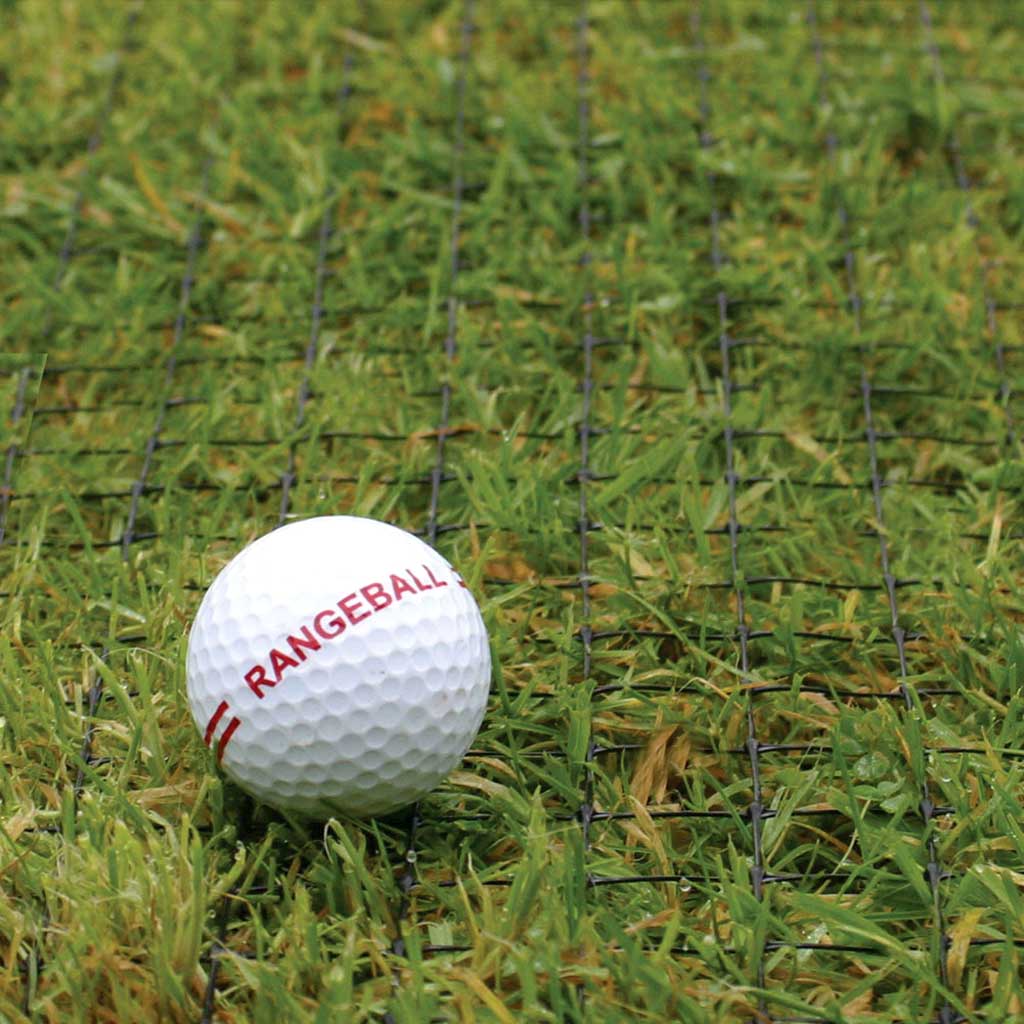 golf ball with red writing saying 'rangeball' on it lying against anti-ball plugging net on top of grass