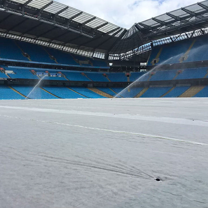 germination sheet laid out on a stadium floor with water being sprayed over it. surrounded by blue seats