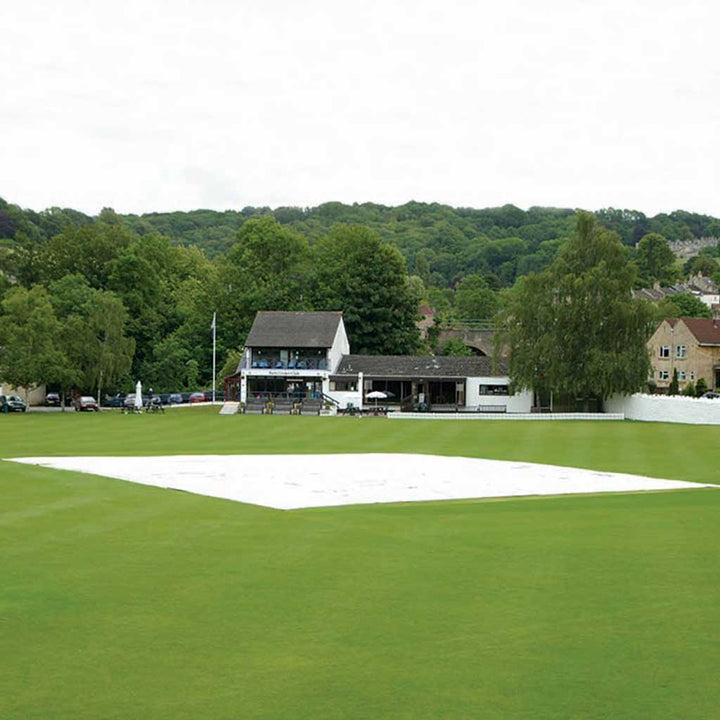 rain cover over cricket pitch with houses and trees in the background