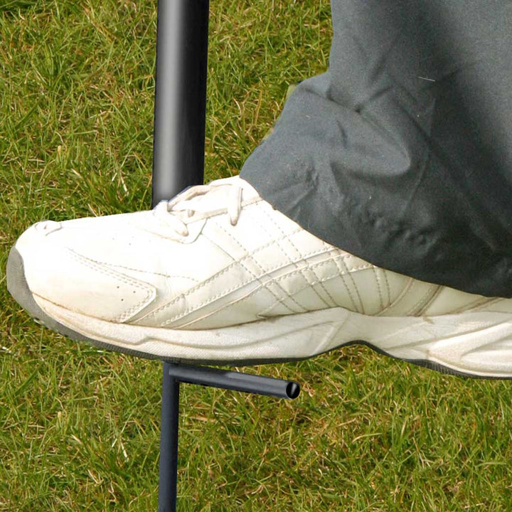 close up of a white tennis shoe pushing a pole into grass