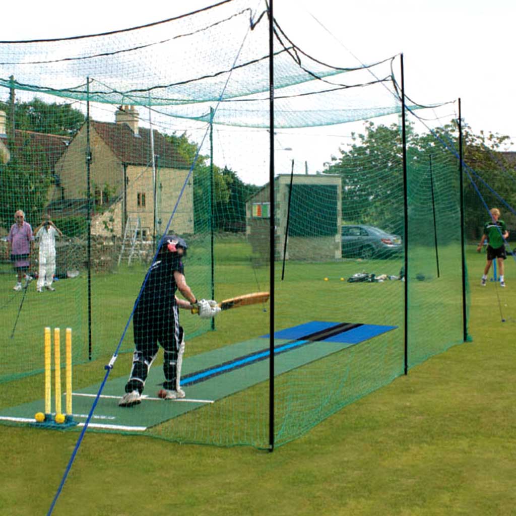 Cricket players playing cricket inside a green practice cage with roof