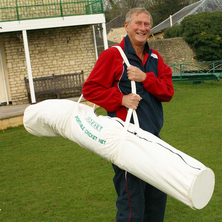 smiling man in a red and black sweater holding a white portable cricket net bag with the cricket net inside. 
