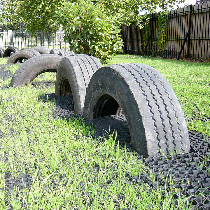 Stack of used tires on grass with a fence and trees in the background